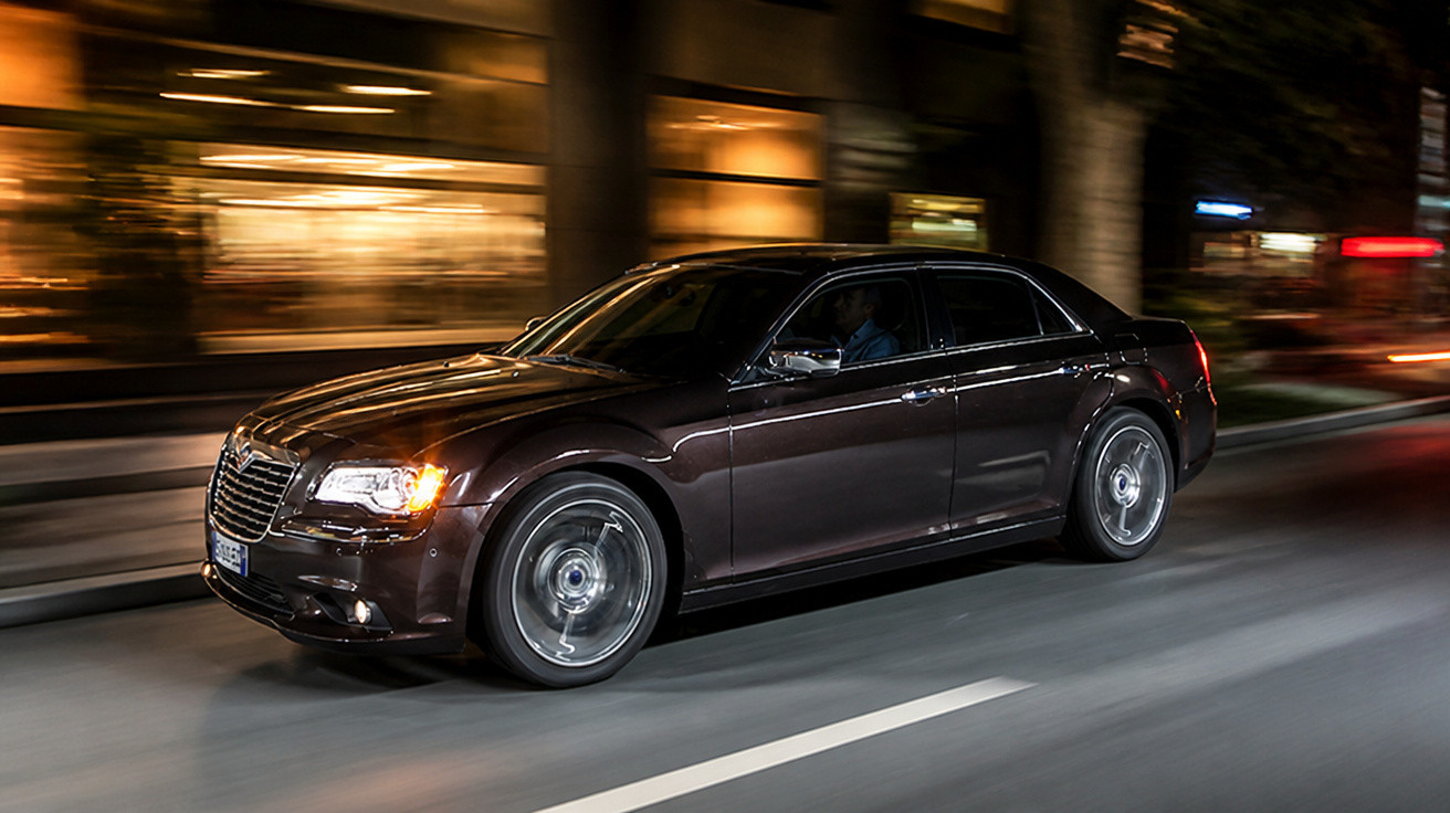 Black luxury saloon car driving fast on city street at night with motion blur on wheels and background