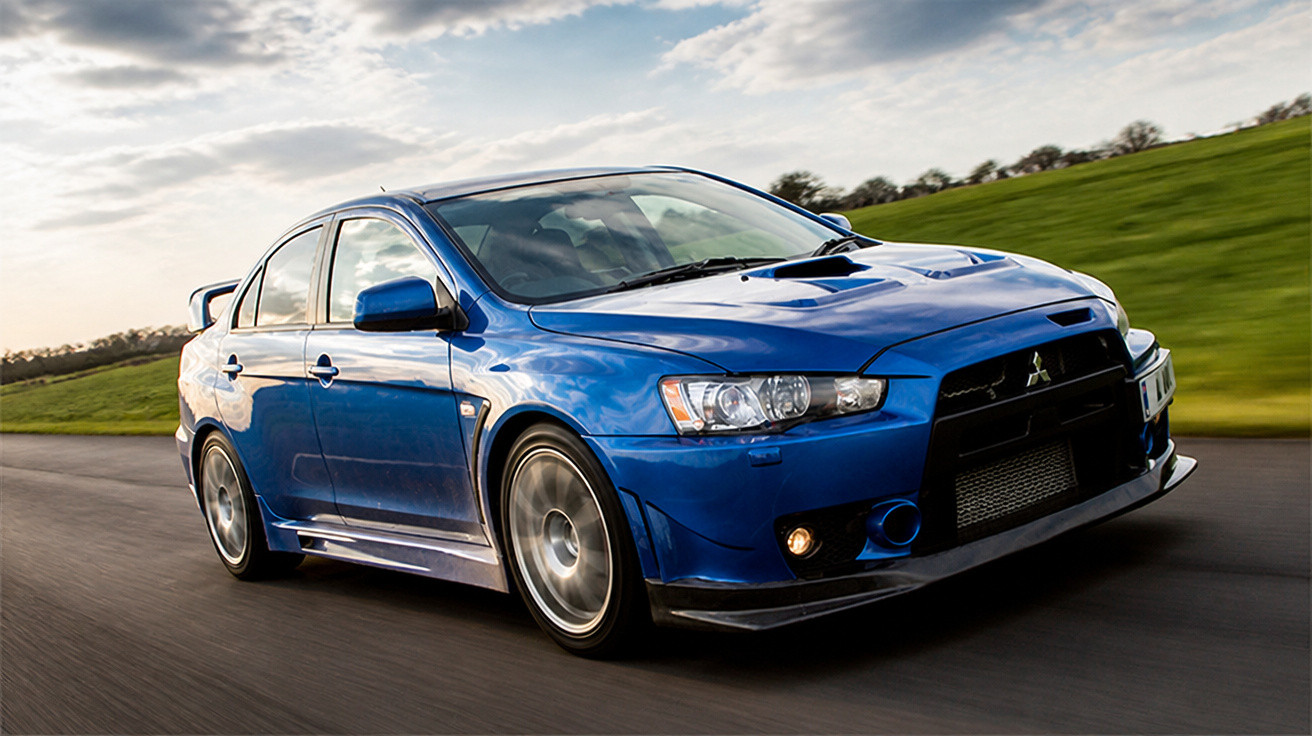 Blue Mitsubishi Lancer Evolution sports car speeding on a countryside road under a cloudy sky.