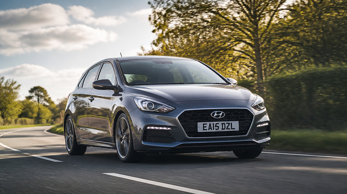 Grey Hyundai i30 hatchback driving on a tree-lined country road under a partly cloudy sky.