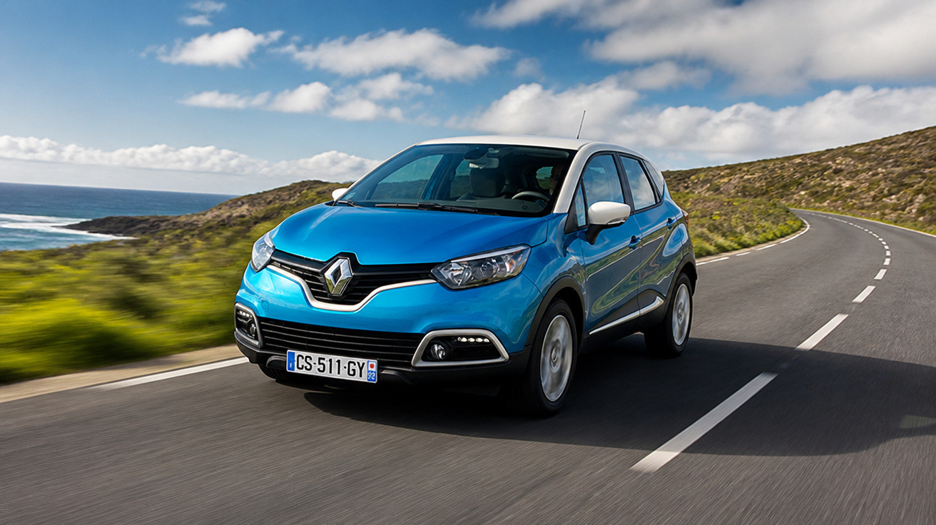 Blue Renault Captur driving on a coastal road under a partly cloudy sky with hills in the background.