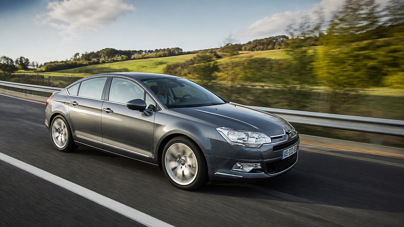 Grey Citroën sedan driving on a highway with green fields and trees in the background.