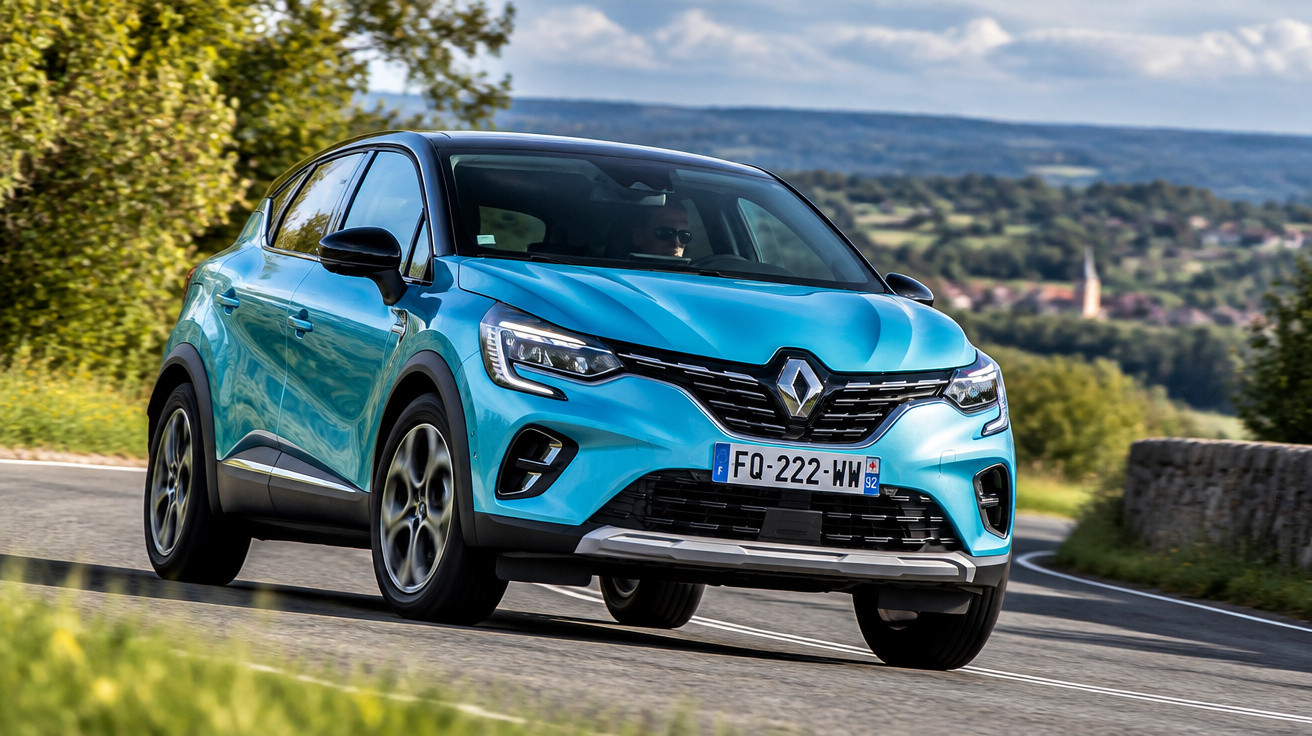 Blue Renault Captur driving on a winding rural road with trees and hills in the background.