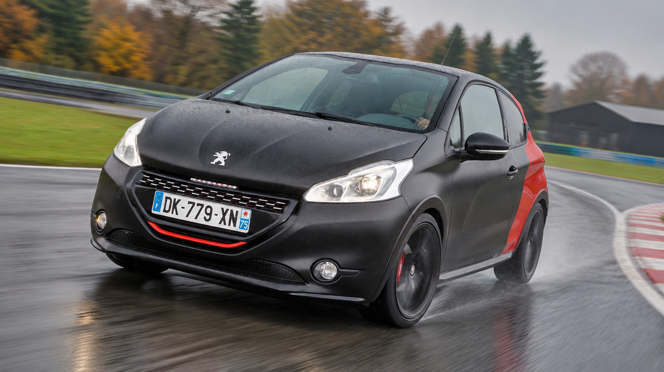 Black and red Peugeot hatchback driving on a wet race track with autumn trees in the background.