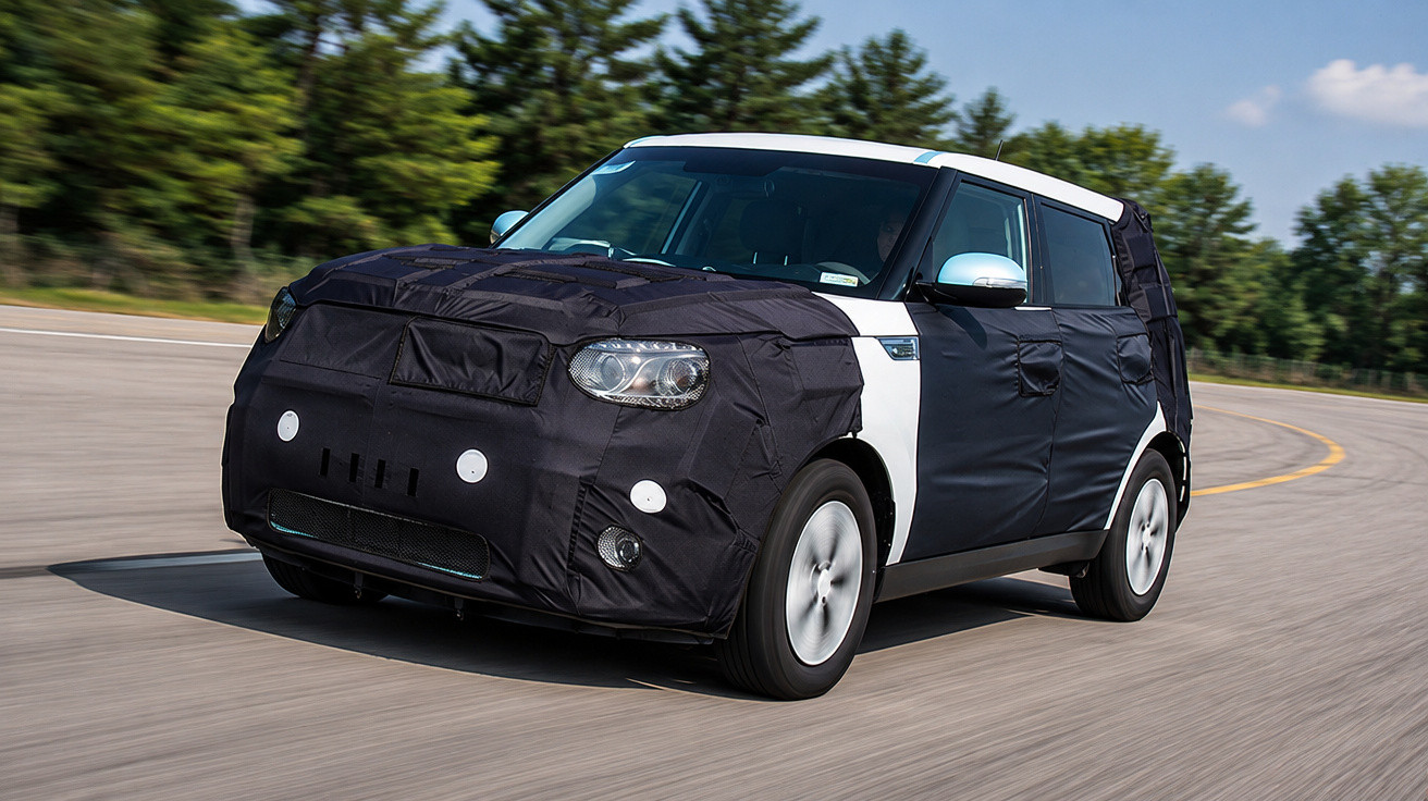 Compact car covered in black camouflage driving on a curved road with trees in the background.