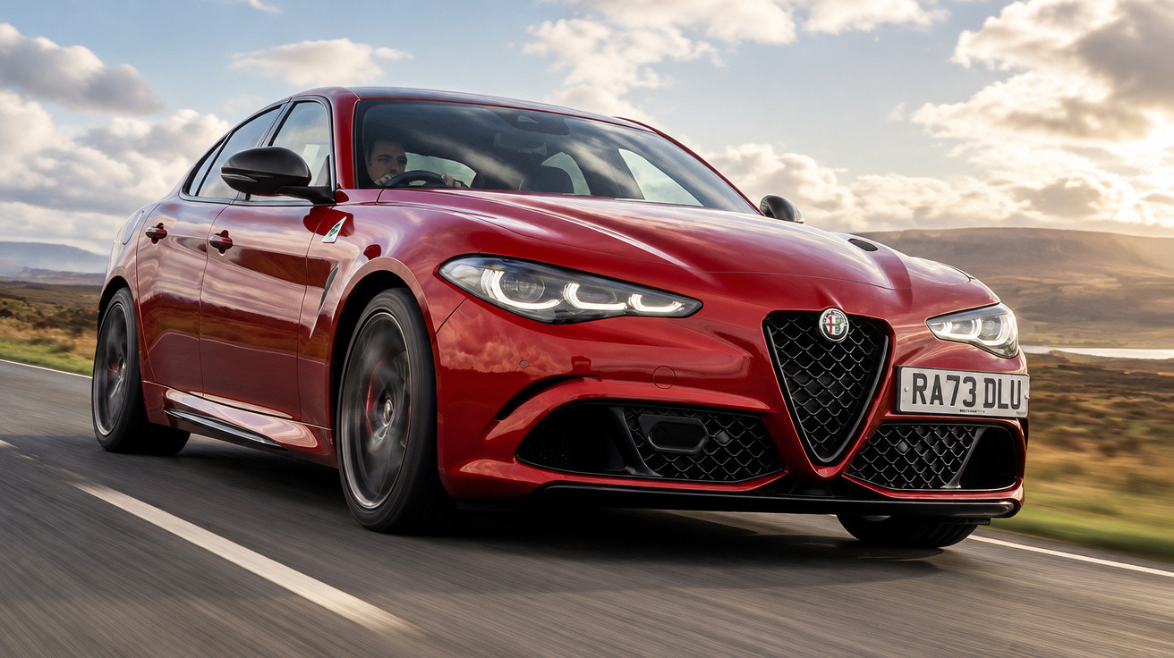 Red Alfa Romeo sedan driving on a countryside road with cloudy skies in the background.