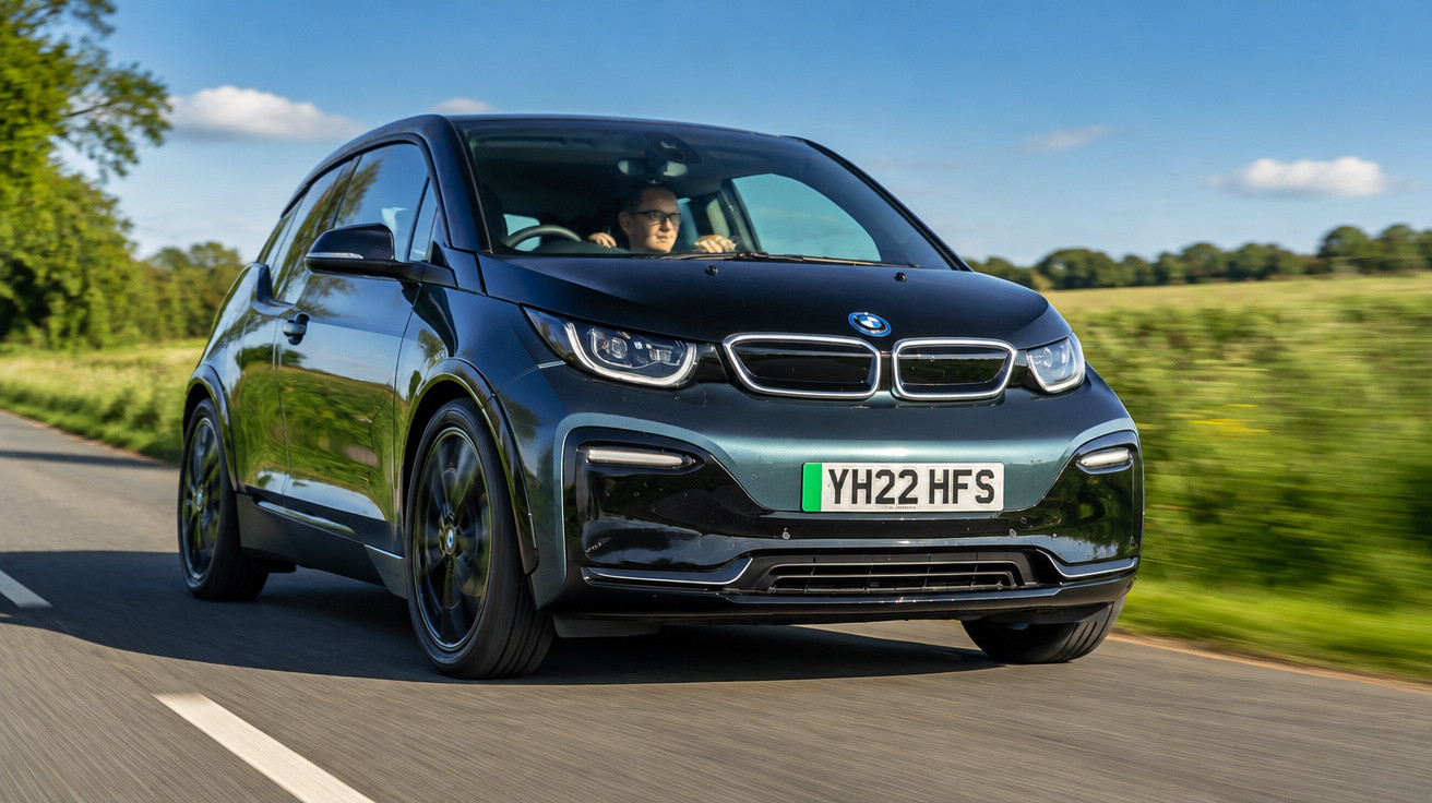 Black BMW i3 electric car driving on a country road with a driver visible inside.